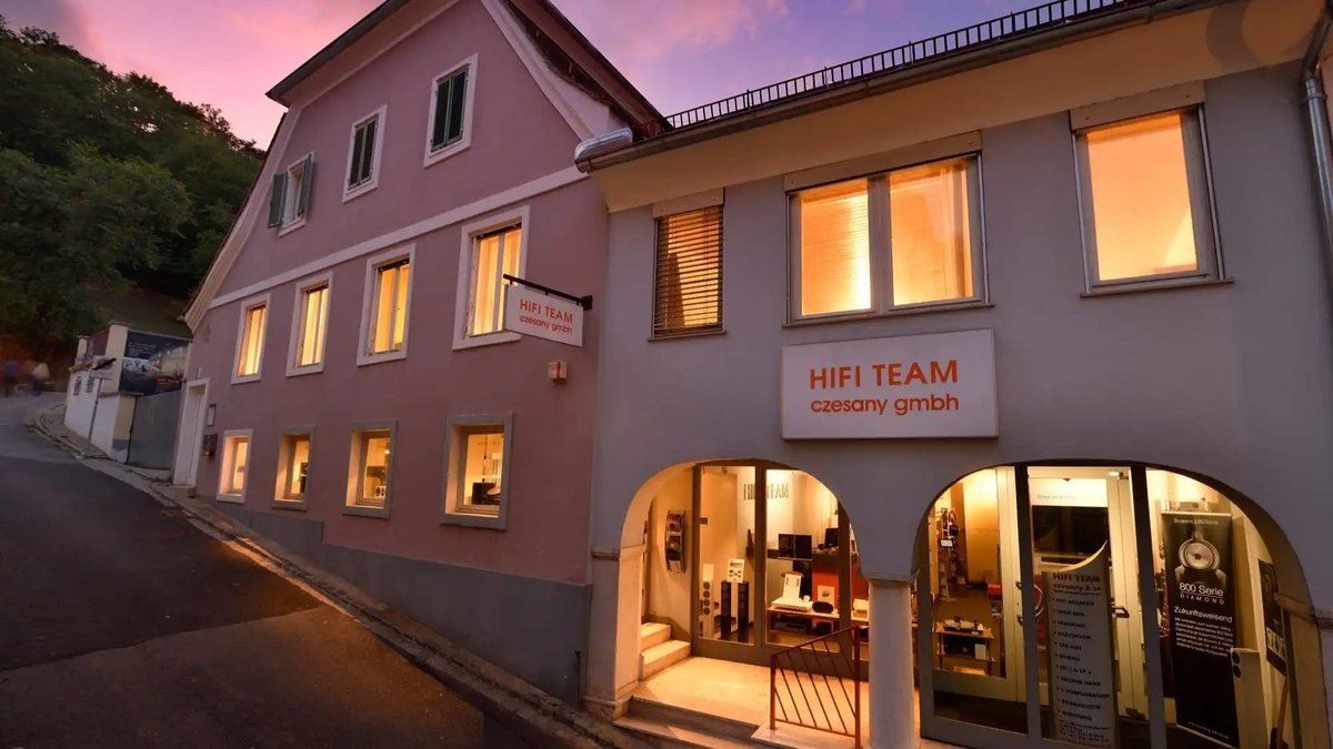 Geschäft von HIFI TEAM am Fuße des Schloßberges in Graz, Fassade mit beleuchteten Schaufenstern in der Abenddämmerung